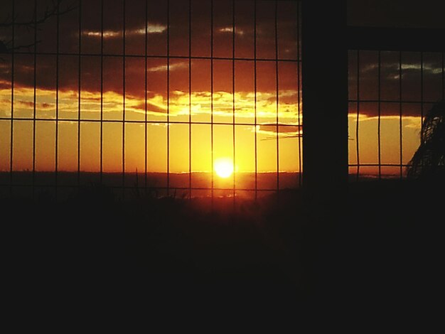 Shining sun seen through fence during sunset