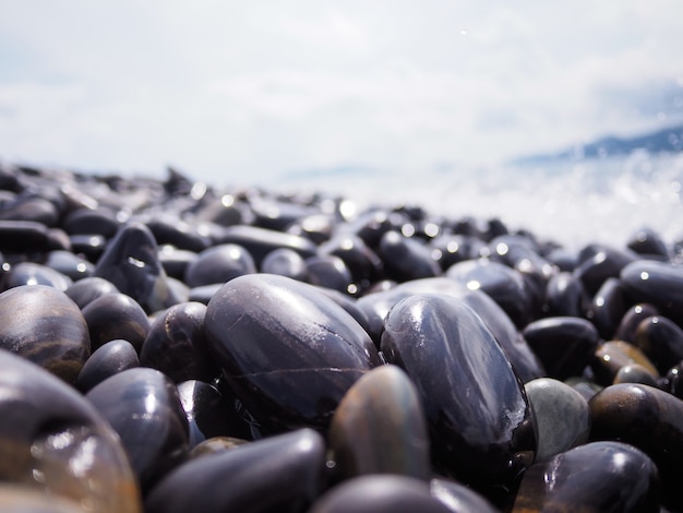 Shiny black stones on the beach with the sea wave attack