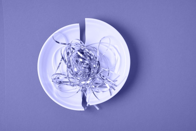 Фото Блестящая праздничная мишура на сломанной белой тарелке, фиолетовый фон