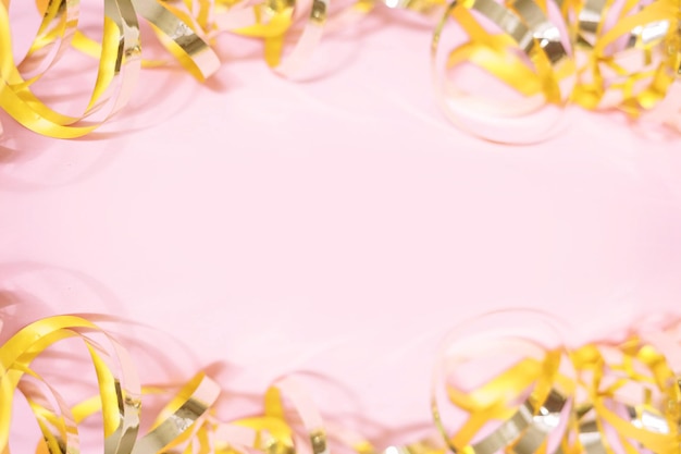 Shiny golden serpentine streamers on pink background with copy space. Top view, flat lay