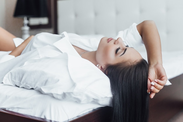 Shiny hair Portrait of a beautiful happy brunette girl in bed on her back.