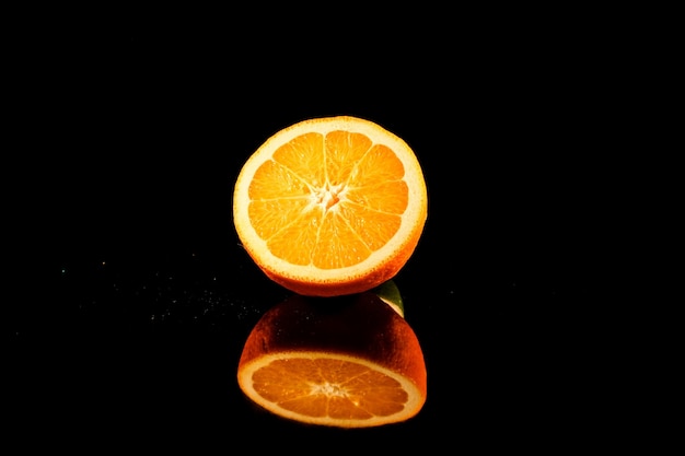 写真 オレンジの光沢のある半分は、黒の背景に黒いガラスのテーブルの上に立つ