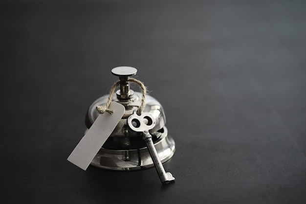 A shiny silver metal bell at the hotel reception. A table in the hotel at the concierge with a bell and a door key. Key and bell in a hotel.