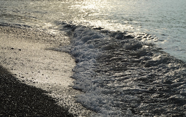 海の小石のビーチ、早朝の日の出に光沢のある銀の水