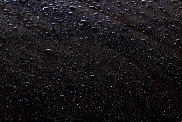 Shiny water drops on black surface, background abstract