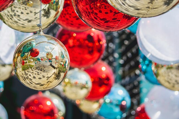 お祝いのカラフルなボケ味の上にモミにぶら下がっている光沢のあるクリスマスガラスのつまらないボール