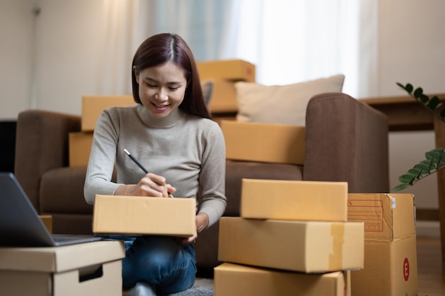 Shipping shopping online young start up small business owner writing address on cardboard box at workplacesmall business entrepreneur SME or freelance asian woman working at home