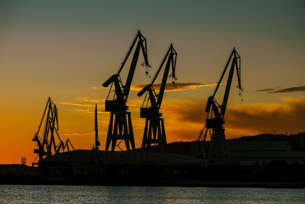 Siluette della gru del cantiere navale contro il cielo arancione del tramonto