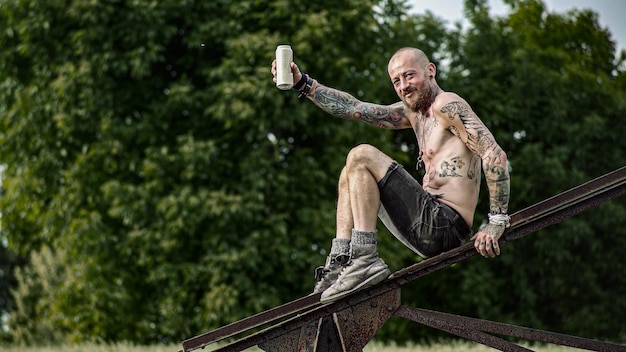 A shirtless bearded man with a tattooed body drinks beer from
the can