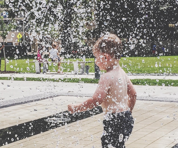 写真 公園で噴水を楽しんでいるシャツのない少年