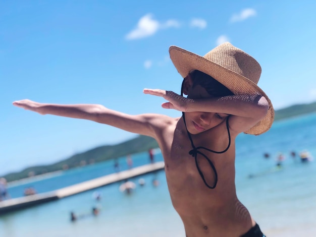 夏の間ビーチに立っている間シャツを着ていない少年が手を振っています
