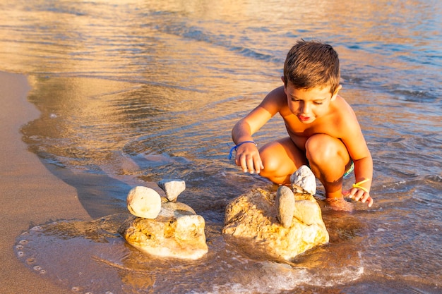 Photo shirtless boy playing with rocks on shore at beach