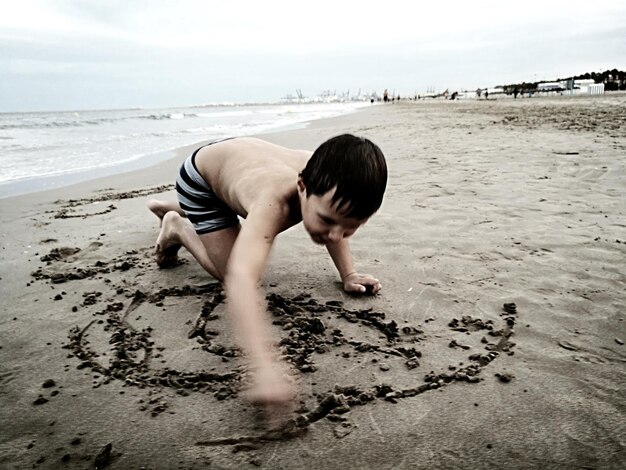 Photo shirtless boy playing with sand at beach