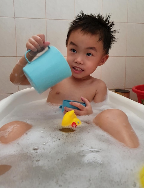 Photo shirtless boy playing with toys in bathtub at home
