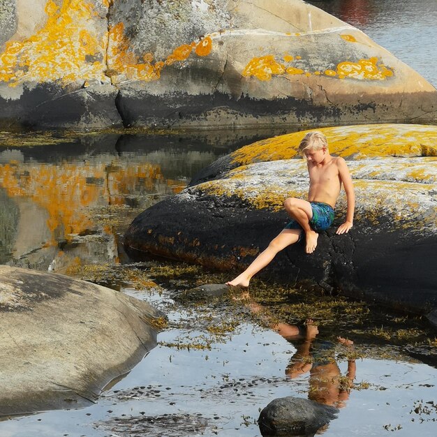 Photo shirtless boy sitting on rock over lake