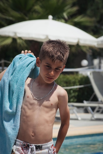 Photo shirtless boy with towel looking down while standing at poolside