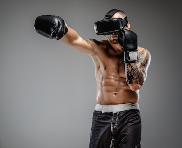 Shirtless brutale boksvechter in virtual reality-bril op zijn hoofd. Geïsoleerd op een grijze achtergrond.