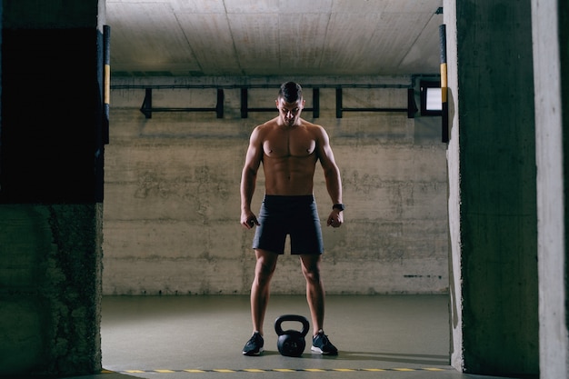 Shirtless Caucasian bodybuilder preparing to lift kettle-bell.