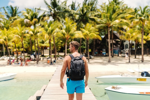 Photo shirtless caucasian man in swimsuit and with backpack walking on pier and looking away.