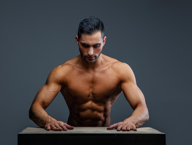 Shirtless gespierde man zit aan de tafel en kijkt naar beneden.