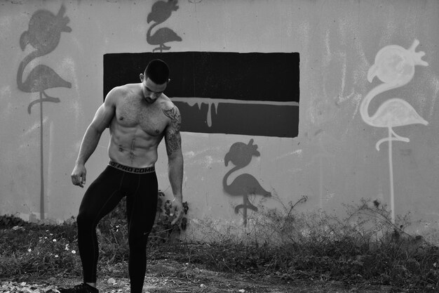 Фото Красивый молодой человек без рубашки стоит на стене с граффити.