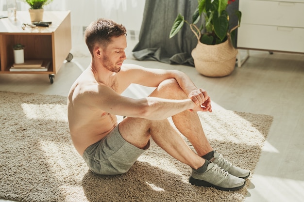 Shirtless jonge atleet die rust op de vloer van de woonkamer na een zware training in de ochtend terwijl hij thuisblijft voor quarantaine