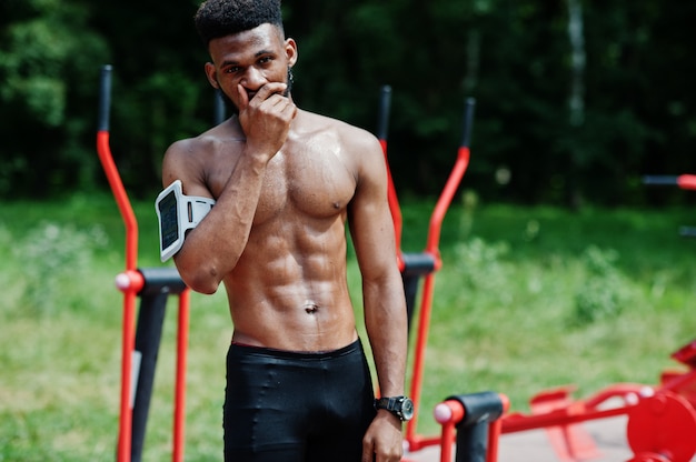 Shirtless male athlete with running sports arm case for mobile phone, doing exercises on the street workout simulators