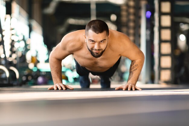 シャツを脱いでジムでプッシュアップをしている男性