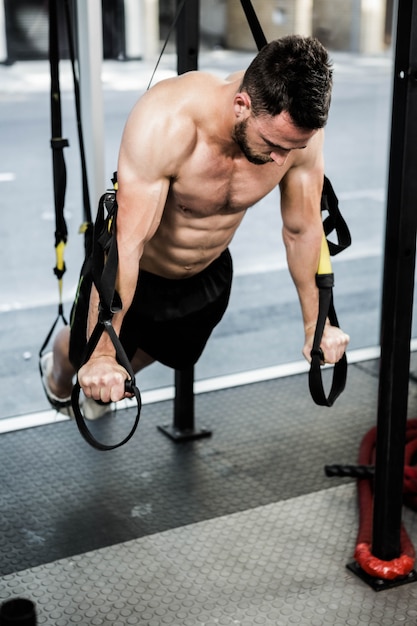 Shirtless man hanging at the rope at the crossfit gym