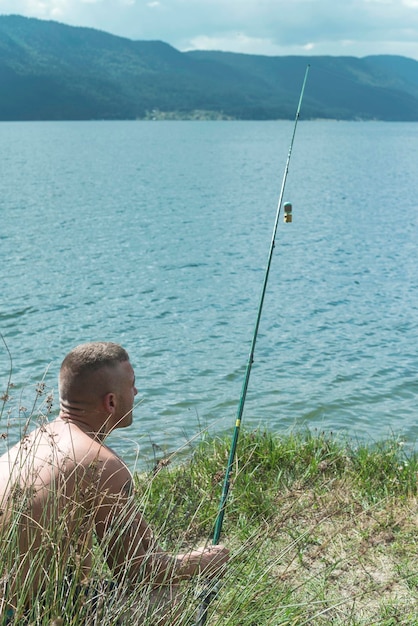 Фото Человек без рубашки с рыболовной палкой у озера на поле
