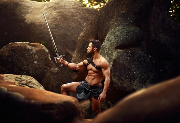 Shirtless man holding sword while standing by on rock