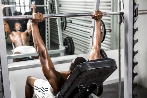 Shirtless man lifting barbell on bench at the crossfit gym