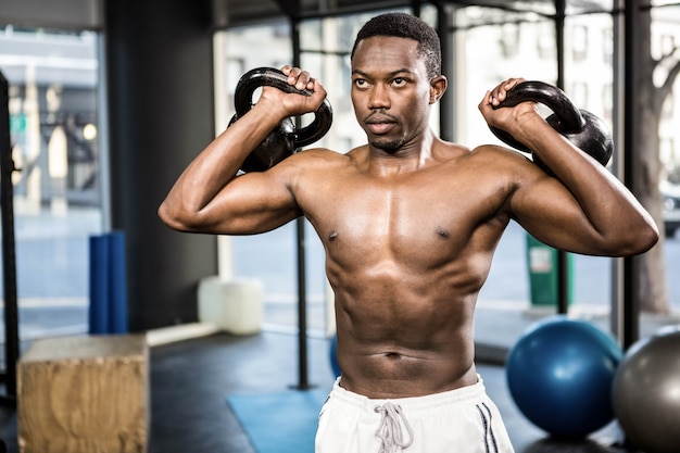 Uomo senza camicia che solleva kettlebells pesanti alla palestra del crossfit