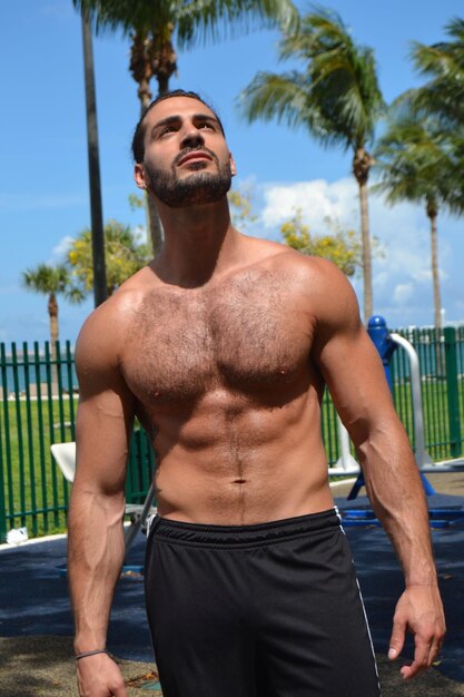 Shirtless man looking up on field during sunny day