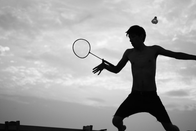 Shirtless man playing badminton against sky