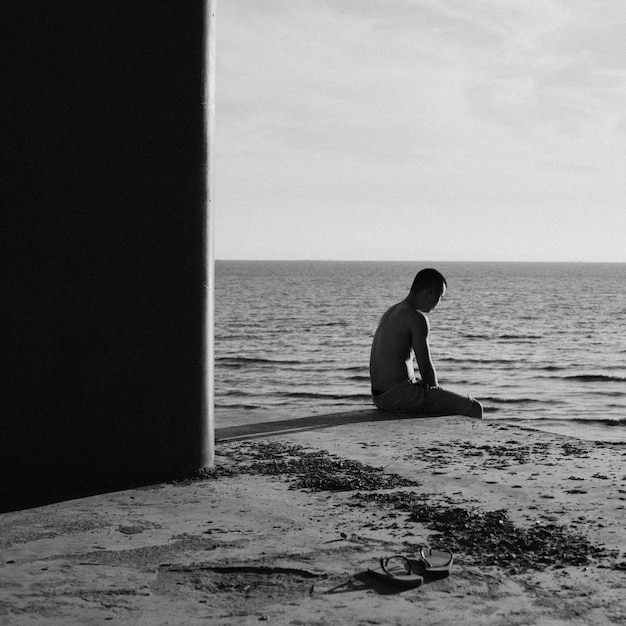 Foto uomo senza camicia seduto sul mare contro il cielo