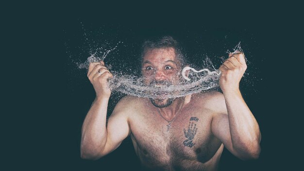 Foto uomo senza camicia che spruzza acqua contro uno sfondo nero