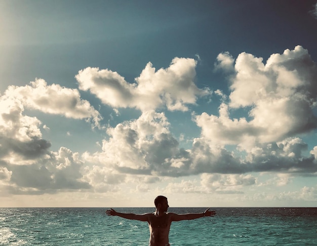 写真 空に向かって海に立っているシャツのない男