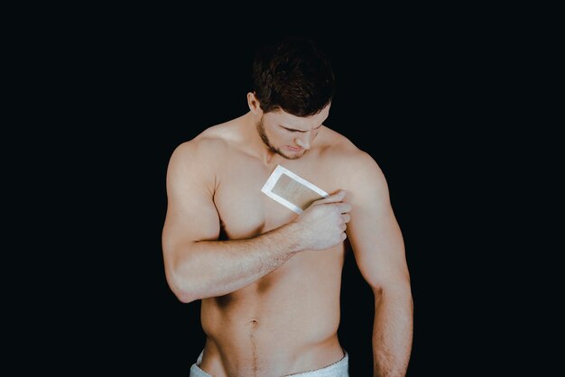 Photo shirtless man sticking adhesive tape on chest against black background