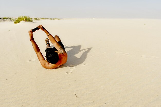 Photo shirtless man taking selfie while lying at desert against clear sky