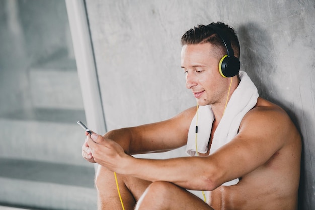 shirtless man using smart phone while sitting by gray wall