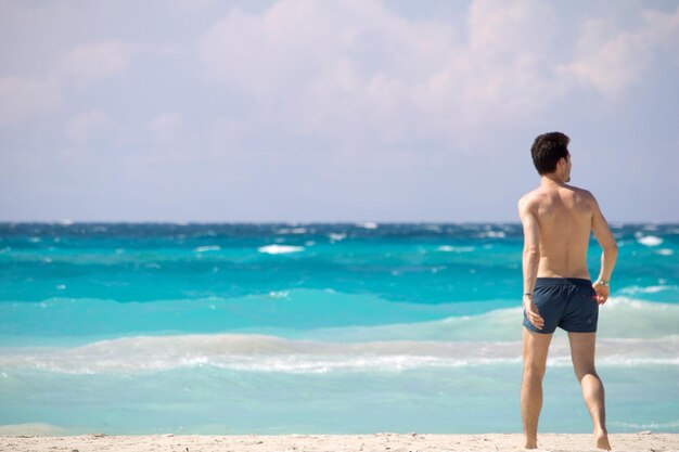 Shirtless man walking at beach against sky