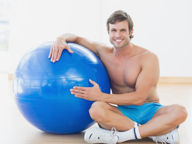 Foto uomo senza camicia con palla fitness in palestra