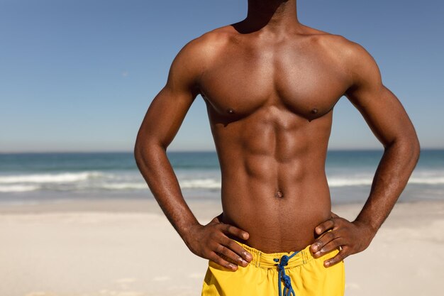 Shirtless man with hands on hip standing on beach in the sunshine