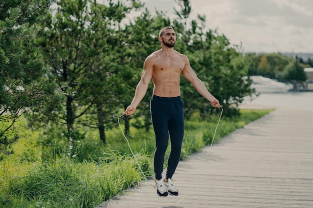 Shirtless man working out outdoors with jump rope