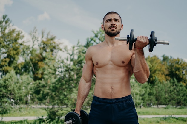 Shirtless man working out outdoors with weights