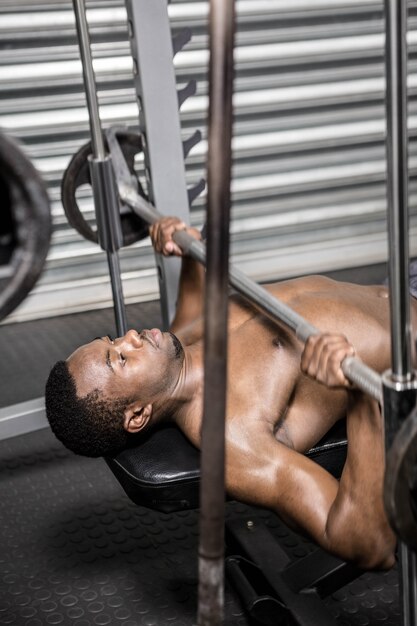 Shirtless mens die barbell op bank opheffen bij de crossfitgymnastiek