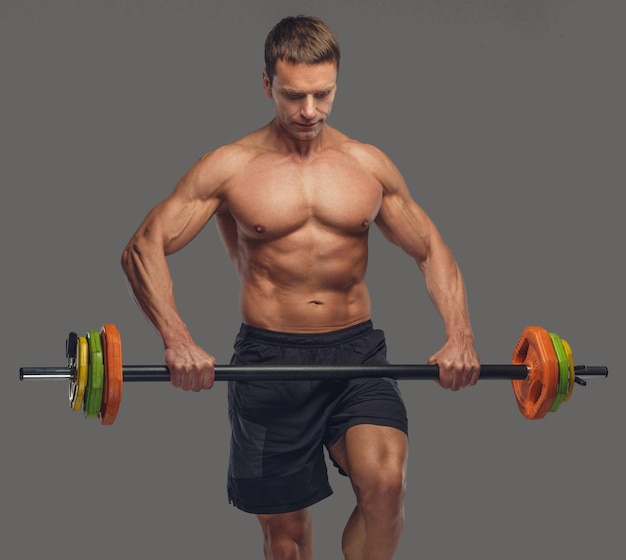 Shirtless middle age male posing with colorful barbell on a grey background.