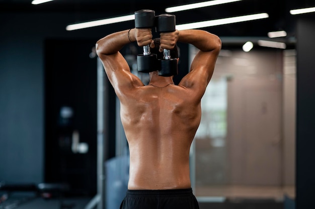 Shirtless muscular african american man training with dumbbells\
at gym interior