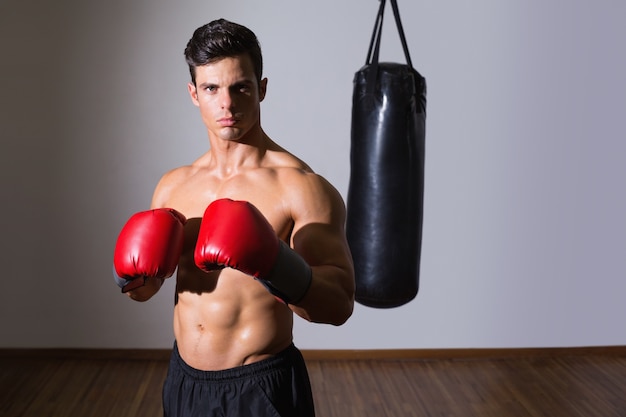 Shirtless muscular boxer with punching bag in gym